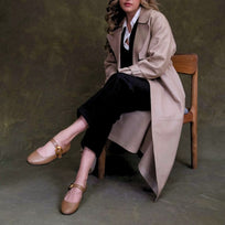 Modelo sentada luciendo balerinas beige con correa y hebilla dorada en look con gabardina