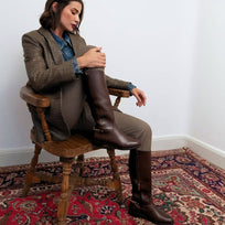 Mujer sentada usando botas altas cafés de Regina Romero en look elegante