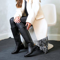 Mujer sentada usando botas altas negras de Regina Romero en look urbano