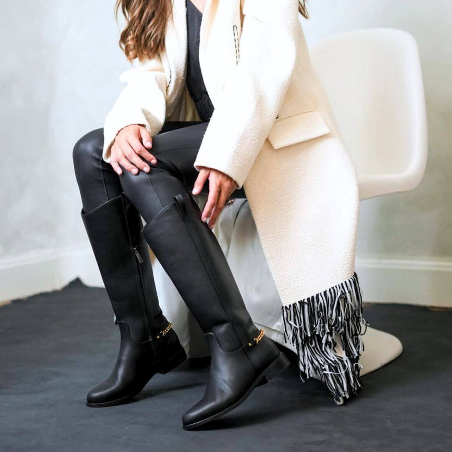 Mujer sentada usando botas altas negras de Regina Romero en look urbano