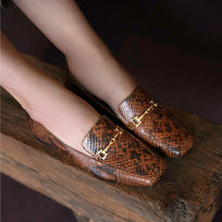 Toma cercana de mocasines con animal print sobre banco de madera, detalle metálico visible