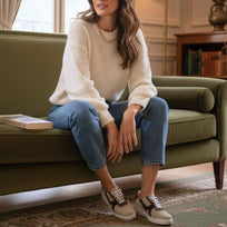 Modelo sentada en sofá luciendo tenis beige y café de Regina Romero