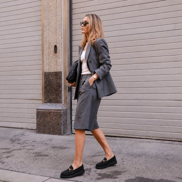 Mujer sentada usando mocasines negros de Regina Romero con herraje dorado